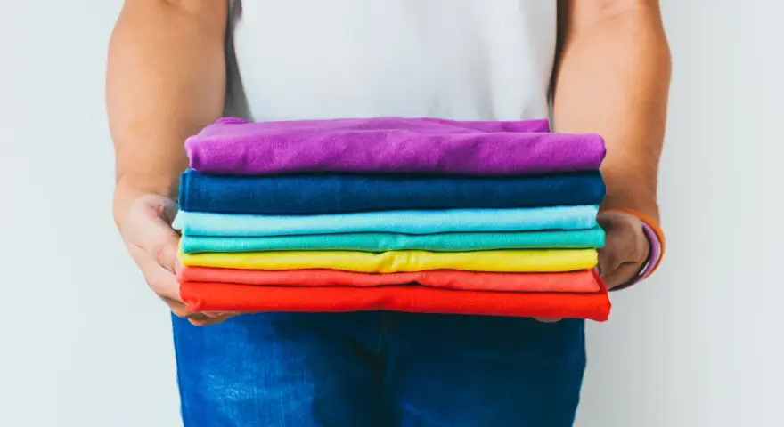 Ein Stapel bunter GSM Kleidung, gehalten von Händen in Jeans.