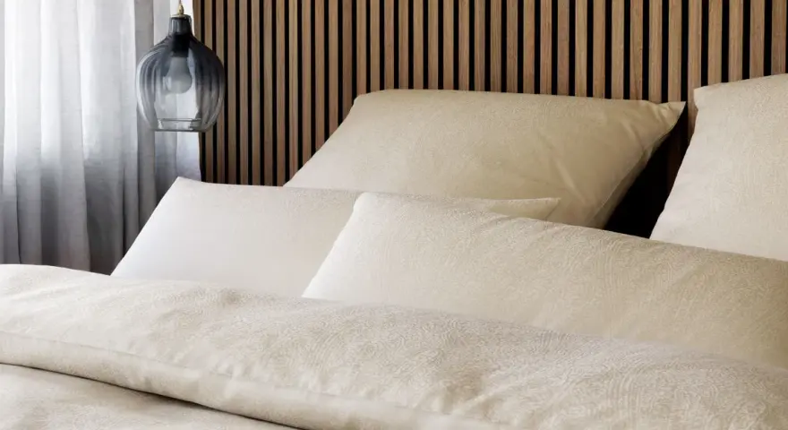 Gemütliches Bett mit Kissen und Decken im dezenten **muster paisley**. Ein moderner Nachttischlampen-Pendel hängt daneben.