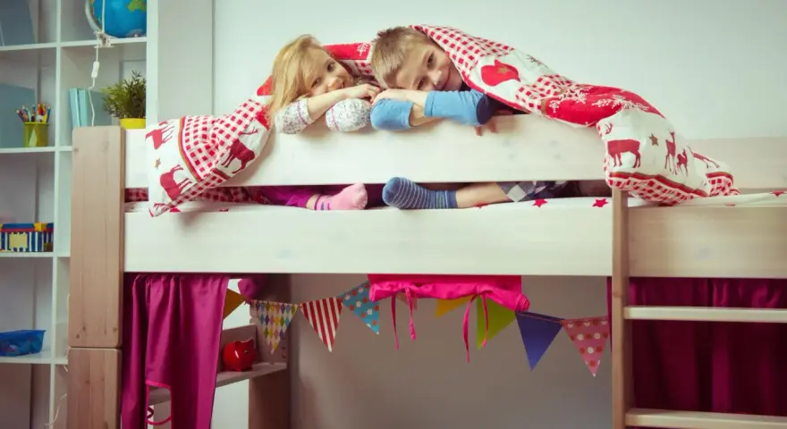 Zwei Kinder kuscheln sich unter einer Decke auf einem Hochbett. Die Frage "Hochbett ab wann?" stellt sich hier nicht, die Kleinen sind begeistert!