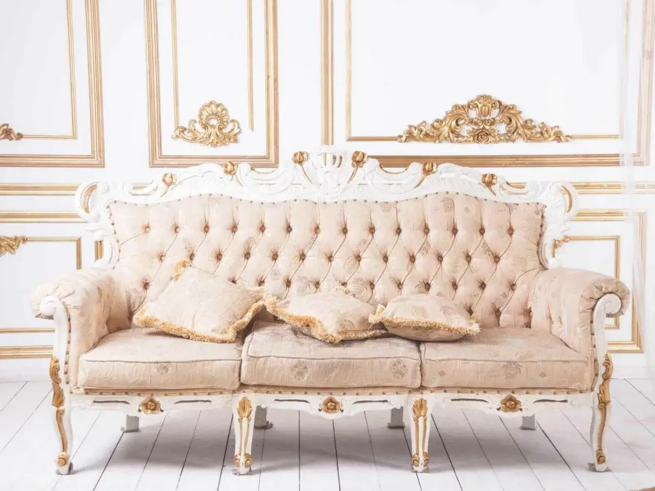 Ein prunkvolles Sofa mit einem zarten muster paisley-Stoff und goldverzierten Elementen, vor einer Wand mit opulenten Goldornamenten.