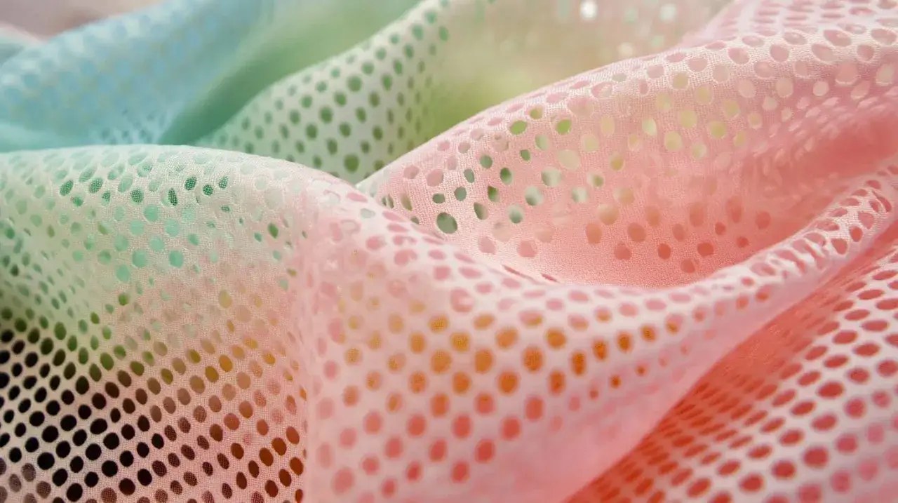 Sanft fallendes, perforiertes mesh textil in Pastelltönen von Rosa und Mintgrün.
