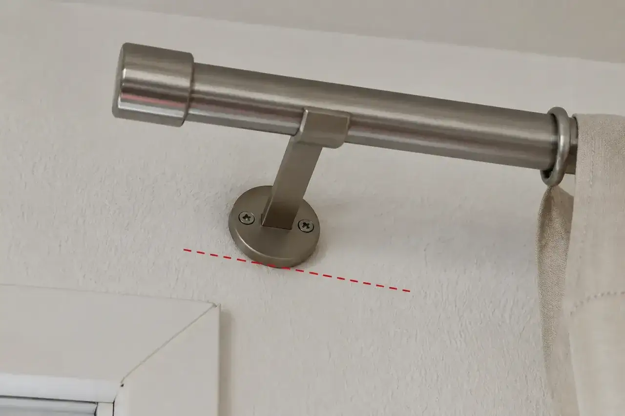 Eine Gardinenstange wird an der Wand befestigt. Die rote Linie zeigt, dass die Montage schief ist.