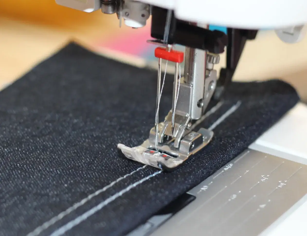 Nähfuß einer Nähmaschine mit doppeltem weißen Faden auf dunklem Stoff, der einen sauberen jersey stich erzeugt.