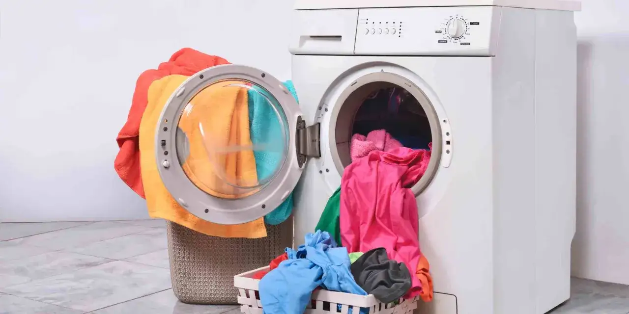 Bunte Wäsche stapelt sich neben einer offenen Waschmaschine. Zeit für die Gardinen zu waschen!
