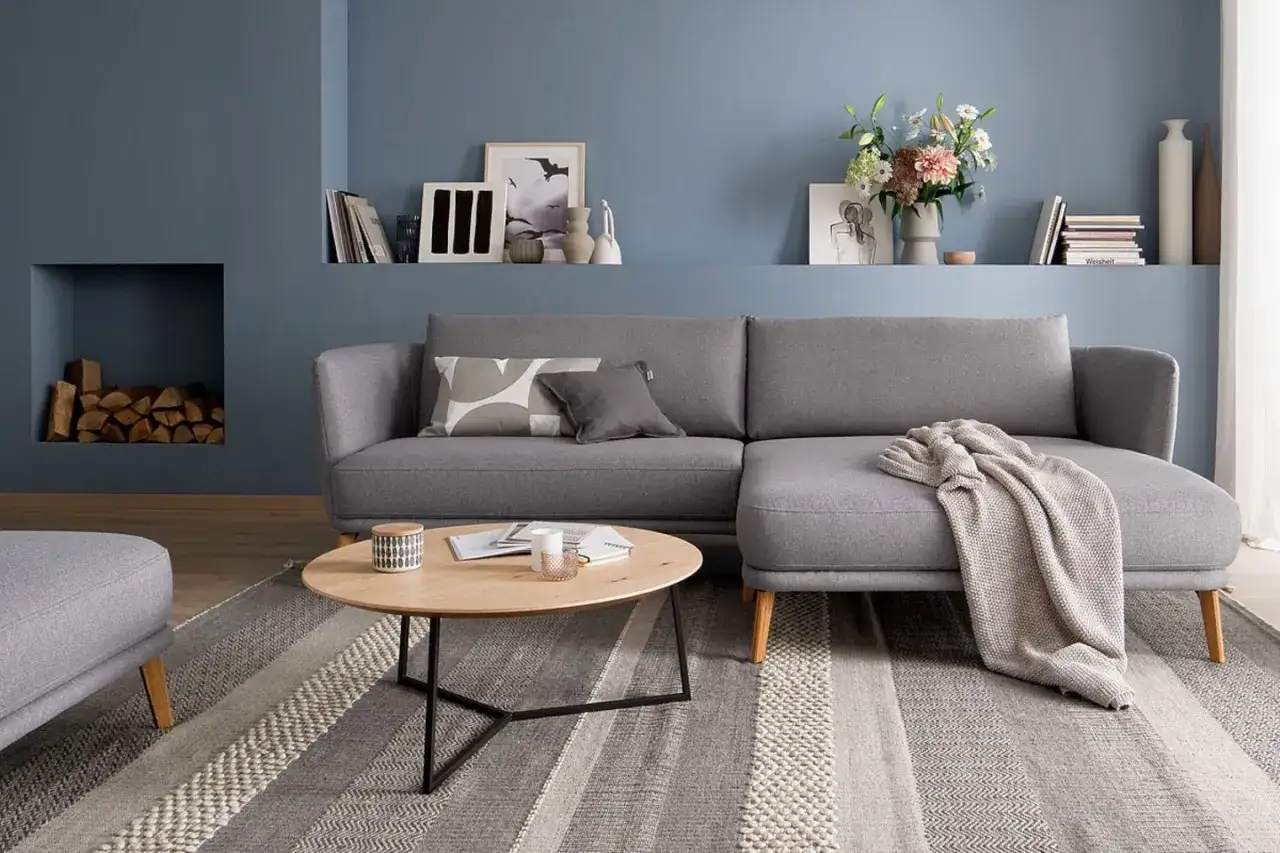 Stilvolle wohnzimmer einrichten ideen: graues Ecksofa, runder Holztisch, gemustertes Teppich und Kamin mit Holz.