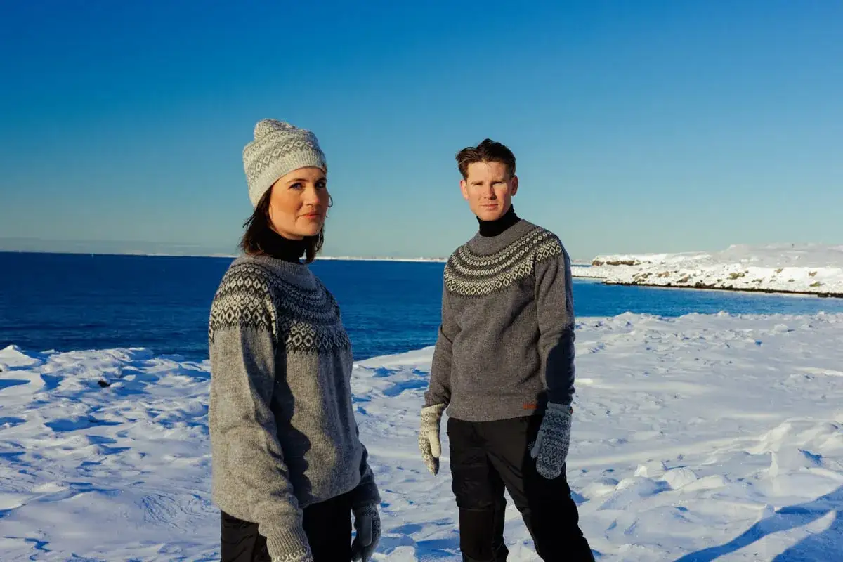 Mann und Frau in winterlicher Landschaft tragen warme Pullover aus Acryl-Stoff. Trotz Kälte schwitzen sie nicht, dank atmungsaktiver Wolle.