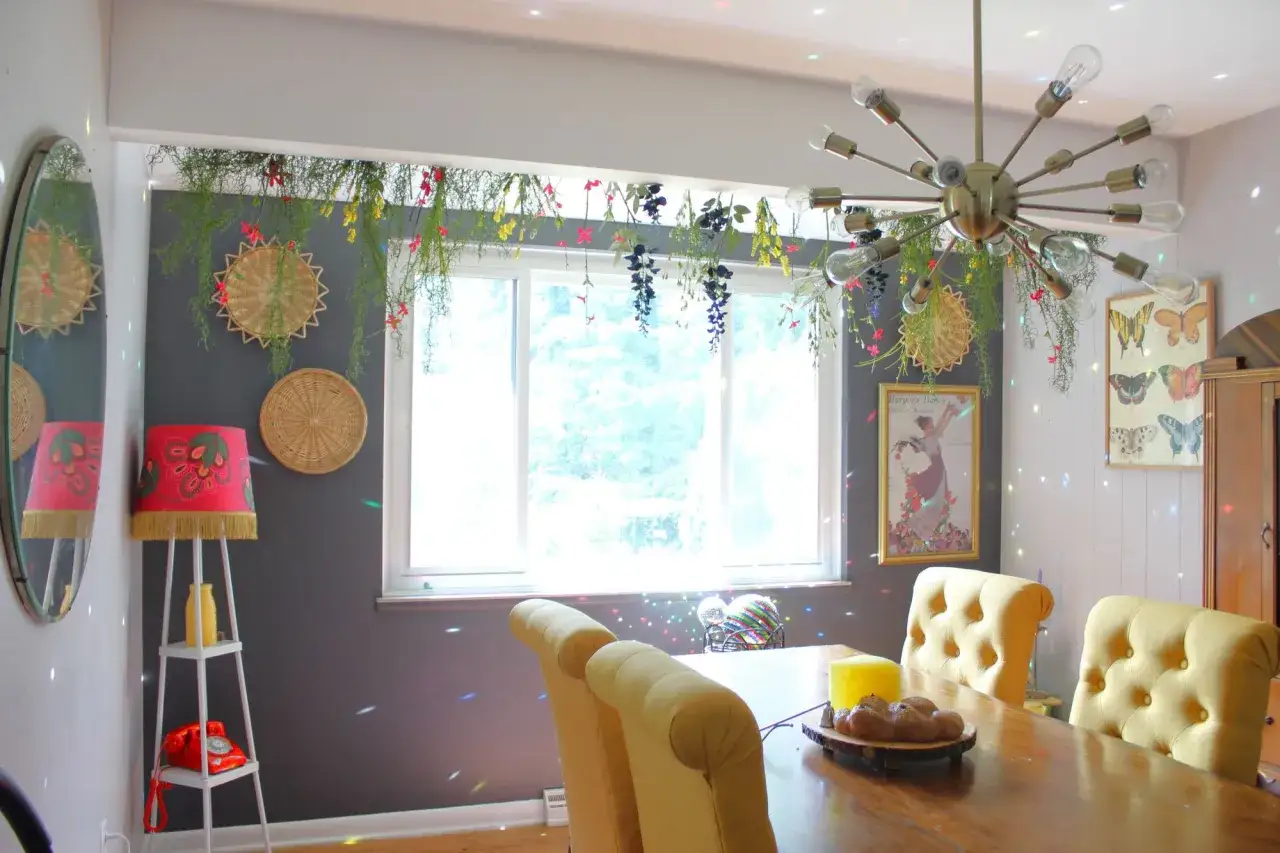 Grüne Ranken und bunte Blumen schmücken die Gardinenstange über dem Fenster. Ein Spiegel und ein auffälliger Kronleuchter vervollständigen die Dekoration.