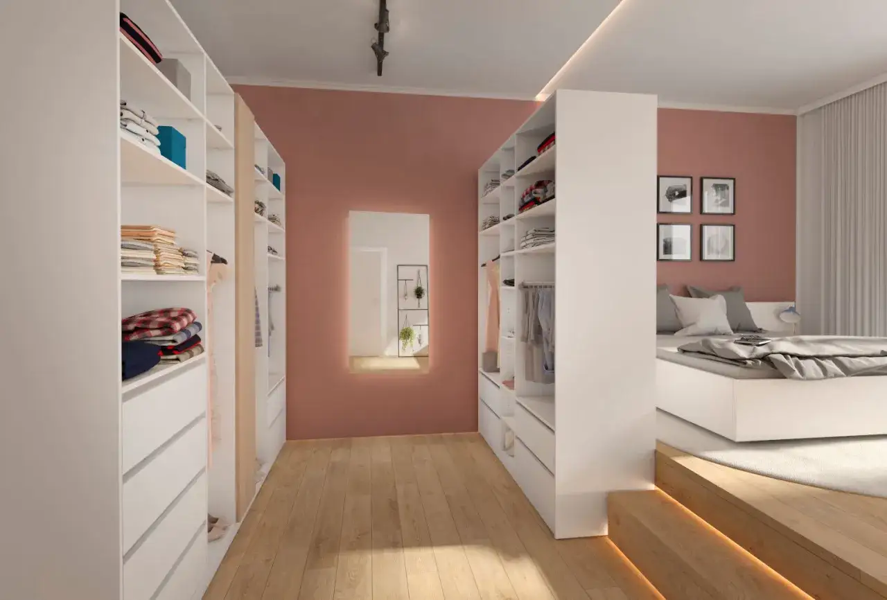 Ein moderner begehbarer Kleiderschrank selber bauen: weiße Regale mit Kleidung und Schubladen, daneben ein Bett.