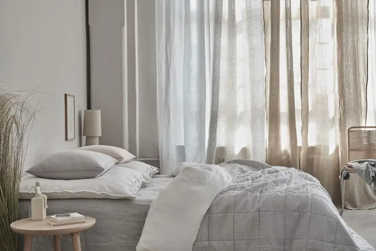 Schlafzimmer mit Bett, Kissen und verschiedenen Gardinen Arten, die das Licht sanft filtern.
