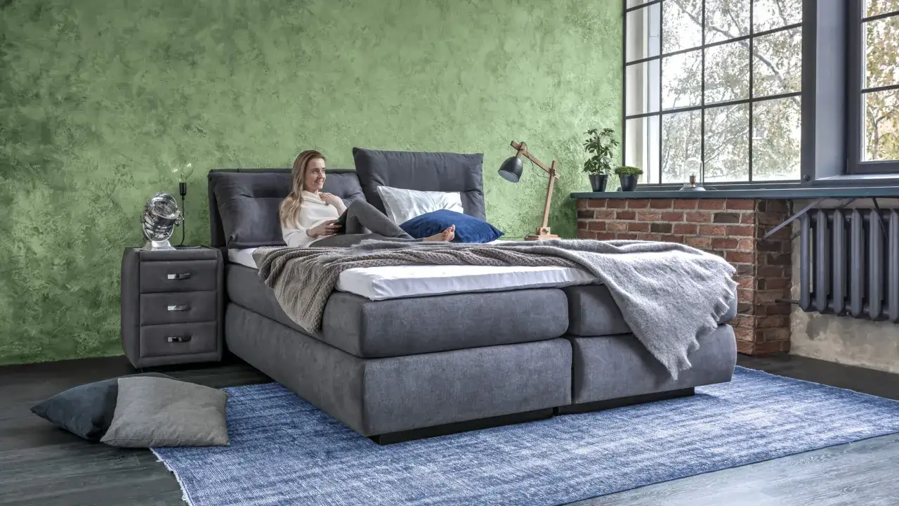 Frau entspannt auf einem modernen Polsterbett. Der Unterschied zum Boxspringbett ist die fehlende Federkernbox.