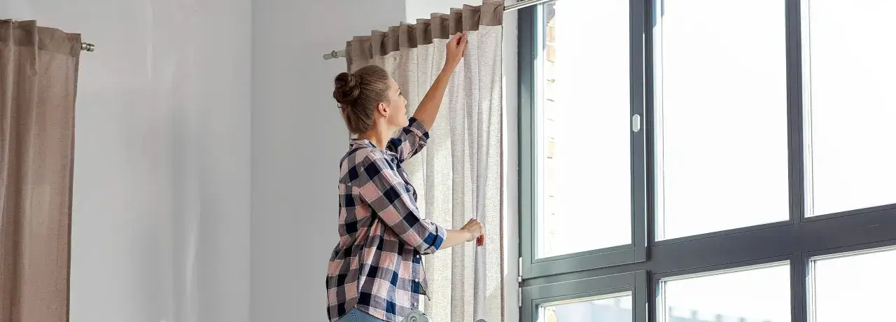 Frau bringt Gardinen an einem Fenster an.