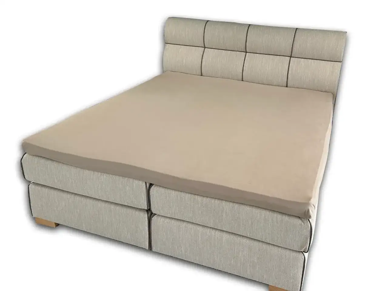 Ein hellbraunes Spannbettlaken wird über eine Matratze eines Boxspringbetts gezogen.