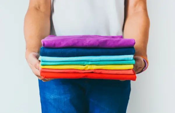 Ein Stapel bunter GSM Kleidung, gehalten von Händen in Jeans.