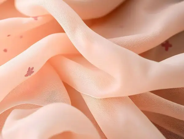 Zartes, pfirsichfarbenes Mesh-Textil mit kleinen, roten Herzchen-Mustern, das sanft fällt und glänzt.