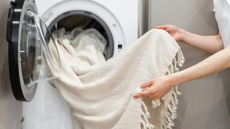 Helle Gardinen werden in die Waschmaschine geladen. Mit Backpulver werden sie wieder strahlend weiß.